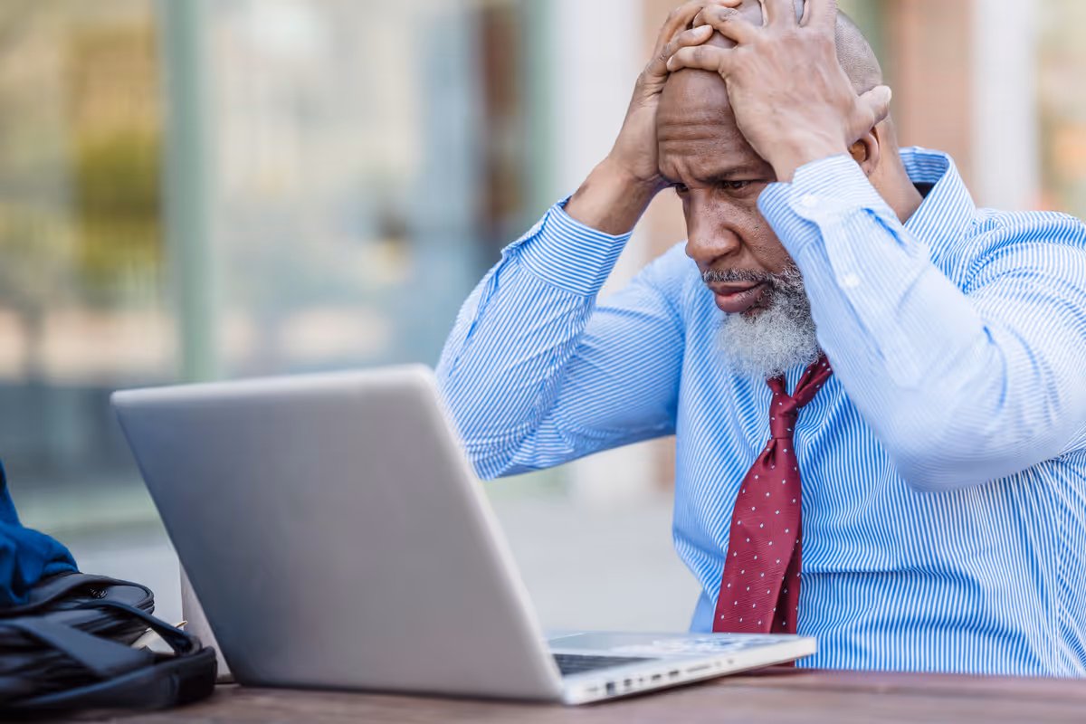 Person at a laptop surrounded by scattered notes and devices.