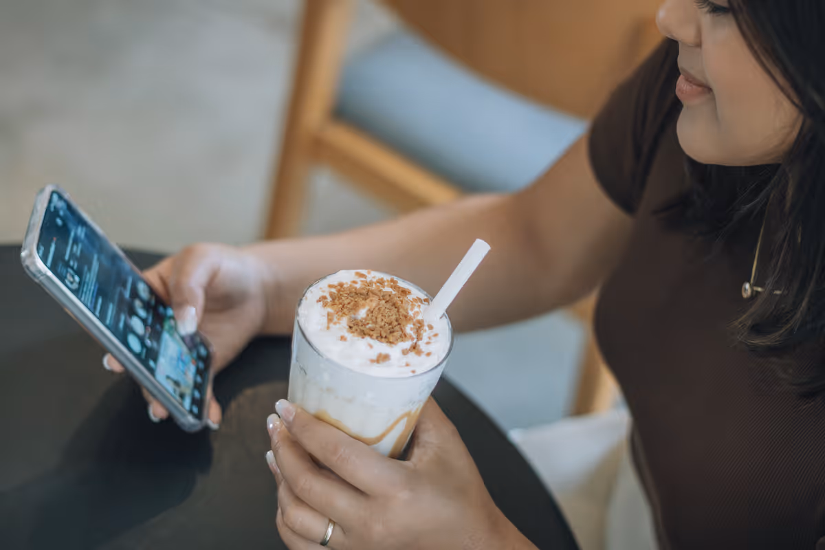 Person scrolling a social commerce feed on a phone in a cafe.